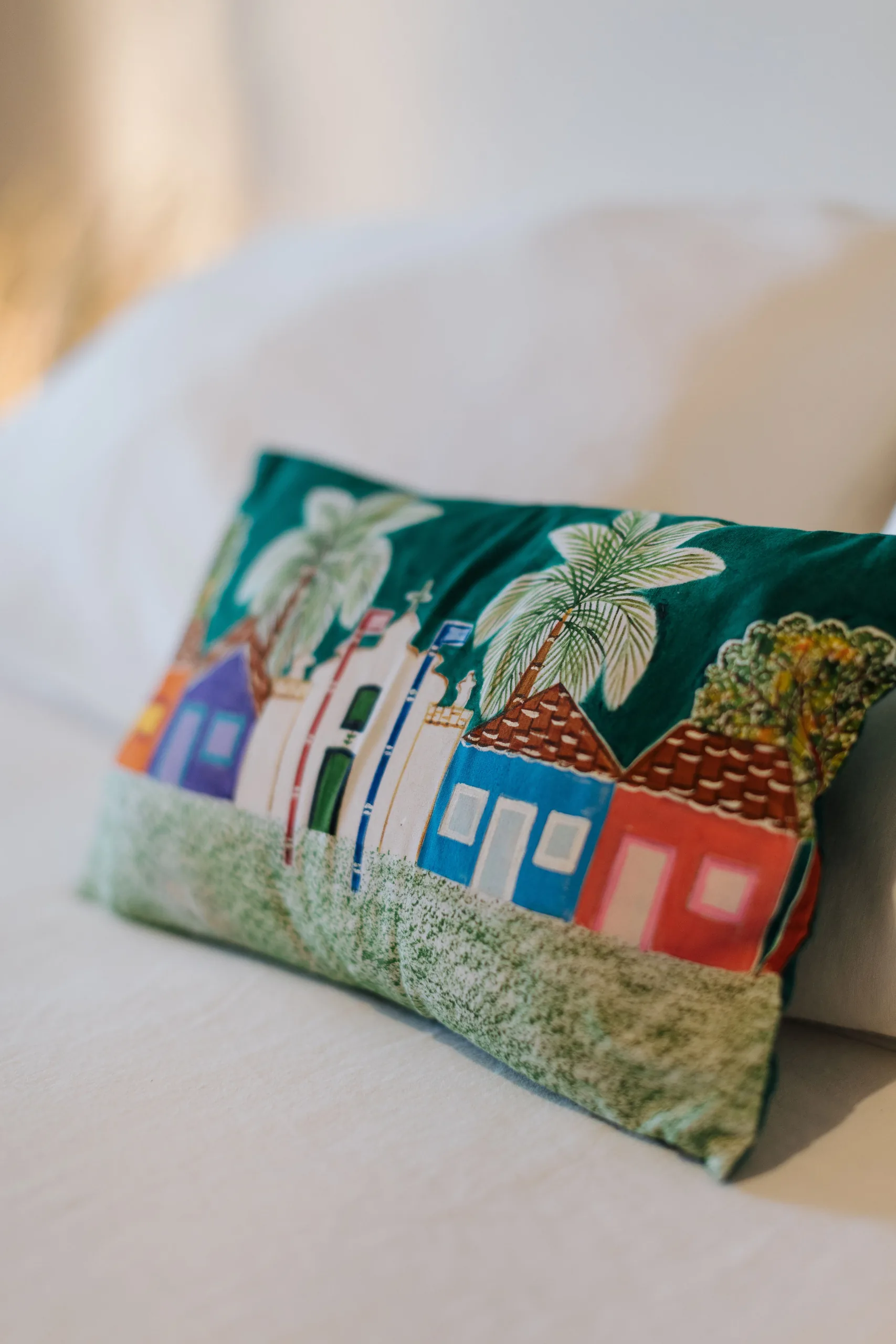 Coussin brodé de petites maisons colorées sur le lit à l’Azorai