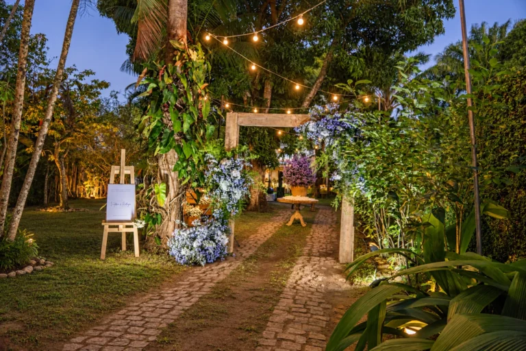 Caminho de pedra no jardim tropical iluminado com luzes e flores para cerimônia de casamento no Azorai