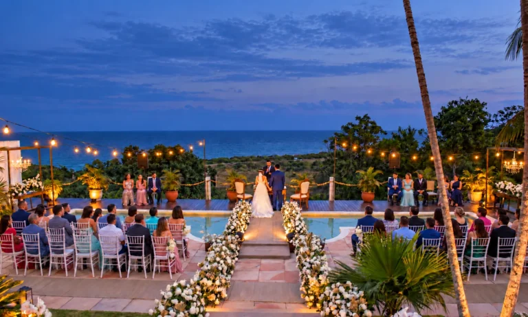 Cerimônia de casamento ao anoitecer junto à piscina, com convidados e o mar ao fundo, no Azorai