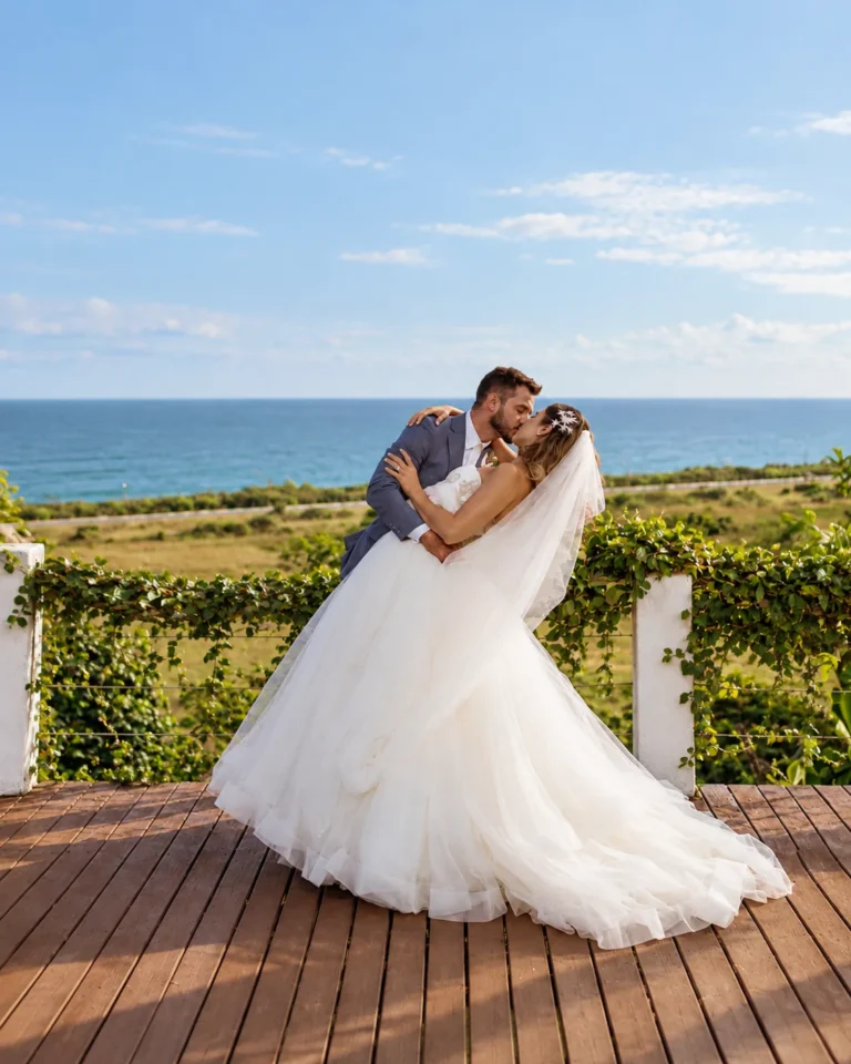 Noivo inclina a noiva para um beijo no deck com vista para o mar, em mini wedding no Azorai, na Bahia