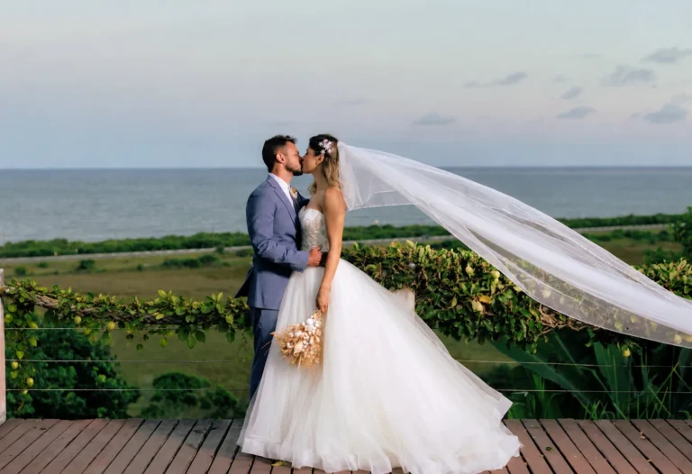 Noivos se beijam no deck com o véu ao vento e o mar ao fundo, em mini wedding no Azorai